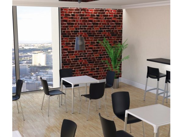 A modern, bright room with large windows providing a cityscape view. The space has wooden floors, a mix of black chairs and white square tables, a brick accent wall, a hanging light fixture, a tall plant, and a high table with bar stools in the corner.