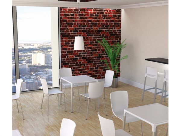 A modern, well-lit lounge area with white tables and chairs, featuring a tall green plant near a red brick accent wall. Large windows show a cityscape view. A white pendant light hangs from the ceiling. Clean, light-colored wooden flooring complements the decor.