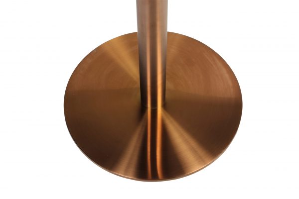 A close-up view of a metallic, circular base of a floor lamp. The surface has a polished copper finish with subtle radial brushing, giving it a sleek and modern appearance. The lamp's vertical shaft is centrally positioned on the base.