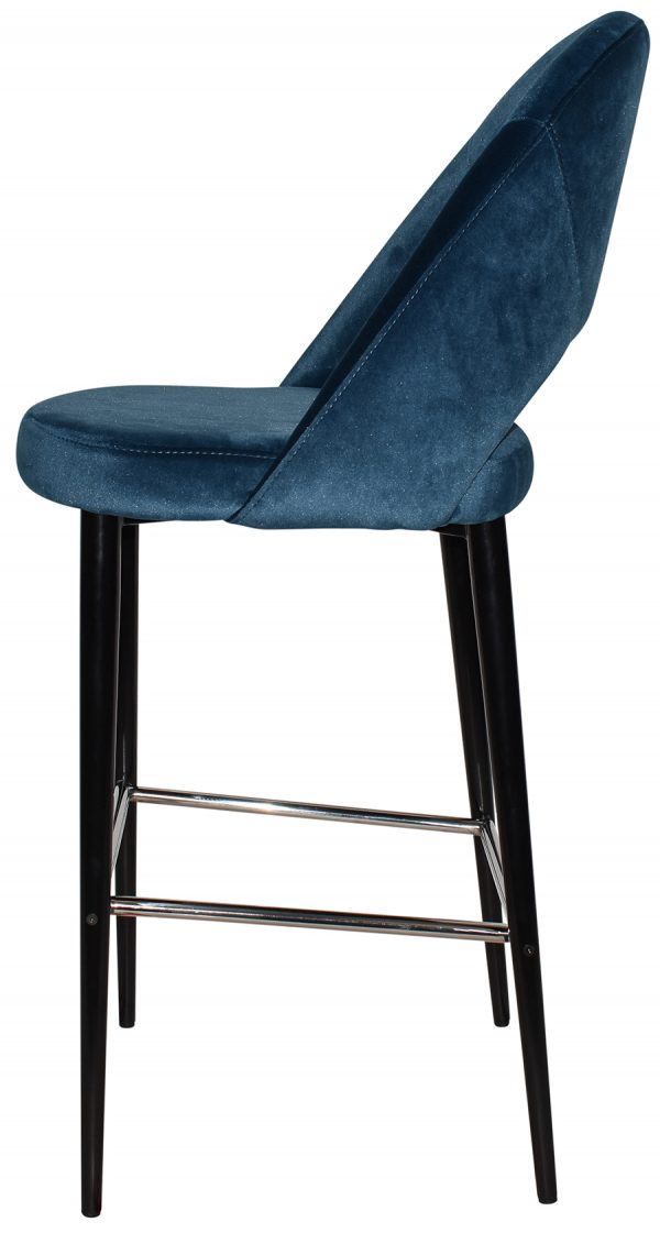 Side view of a modern, blue upholstered bar stool with a triangular backrest, supported by four black metal legs. The legs are connected by two horizontal metal bars for added stability and a footrest. The chair has a sleek, contemporary design.